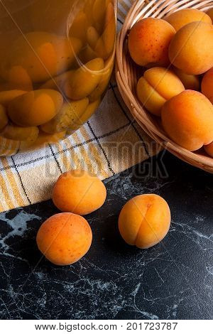 Fresh Organic Harvested Apricots In Basket And Big Glass Jar With Canned Apricot Compote On Dark Mar