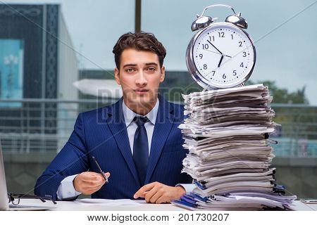 Businessman with pile stack of paper paperwork and an alarm cloc