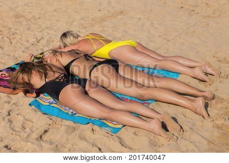 Three blonde girls sunbathing together on beach with sea