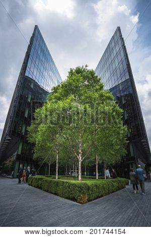 LONDON ENGLAND - JUNE 17 2016: Upward picture of PricewaterhouseCoopers building in London Bridge City in a cloudy day with a tree in the center of the building and people passing by. London.