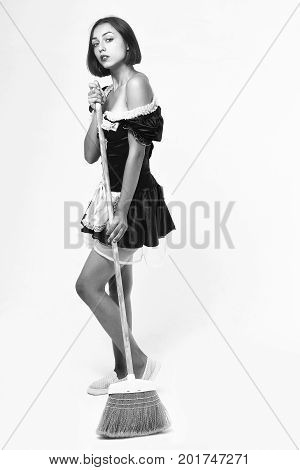 woman with pretty face in parlormaid costume with bare shoulders and lace apron posing with sweep broom black and white