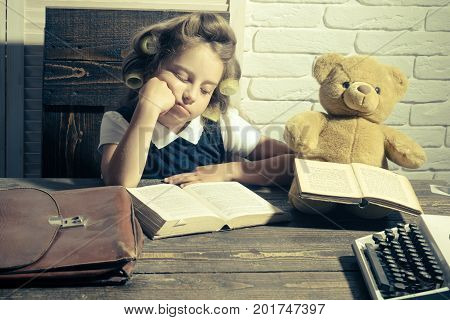 Little baby secretary in cabinet with bear. Kid choose career of journalist or writer. Small girl with curler in hair read book. Child with briefcase and typewriter on table. Education and childhood.