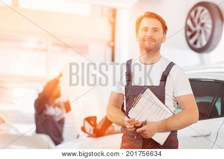 Portrait of confident male maintenance engineer with clipboard in car repair shop