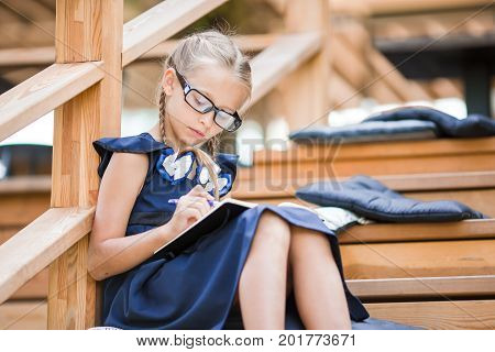 Adorable little school girl with notes and pencils outdoor.