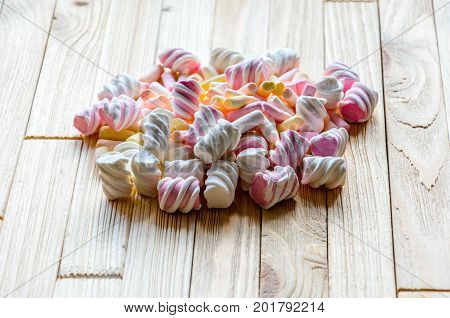 Multicolored marshmallows on bright wooden table. Background of multi-colored and different in shape and size of marshmallows. Sweets background