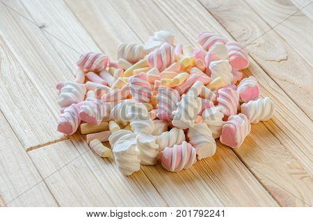 Multicolored marshmallows on bright wooden table. Background of multi-colored and different in shape and size of marshmallows. Sweets background
