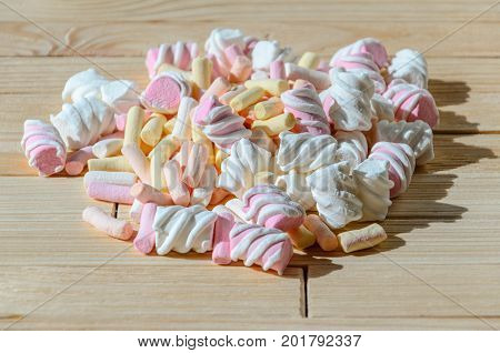 Multicolored marshmallows on bright wooden table. Background of multi-colored and different in shape and size of marshmallows. Sweets background