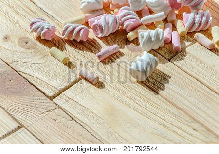 Multicolored marshmallows on bright wooden table. Background of multi-colored and different in shape and size of marshmallows with empty space for text placement