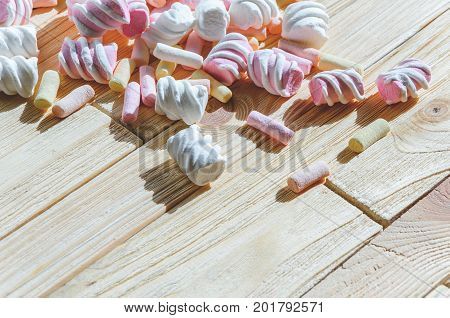 Multicolored marshmallows on bright wooden table. Background of multi-colored and different in shape and size of marshmallows with empty space for text placement