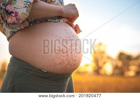 A beautiful pregnant woman on the beach touching her mehandi ornament belly with love and care at sunset lights summer evening