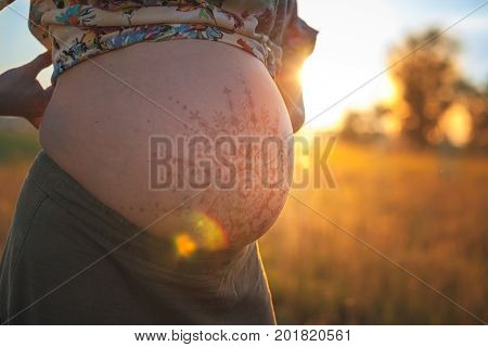 A beautiful pregnant woman on the beach touching her mehandi ornament belly with love and care at sunset lights summer evening
