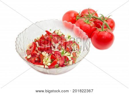 Vegetable salad of the fresh sliced tomatoes white bell pepper onion and potherb in a glass salad bowl against of the cluster of fresh tomatoes on a white background