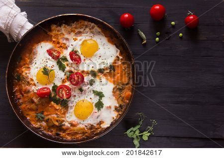 three fried eggs with сherry tomatoes in a pan on a black background with space