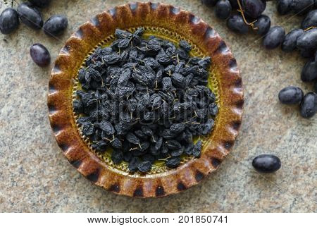 A bunch of fresh sweet dark and succulent raisins poured into a dish grapes lying in a table.