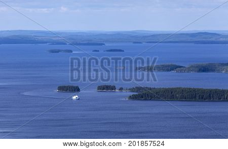 View of a vast lake, islands and islets. White ship approaching, woodland up North.