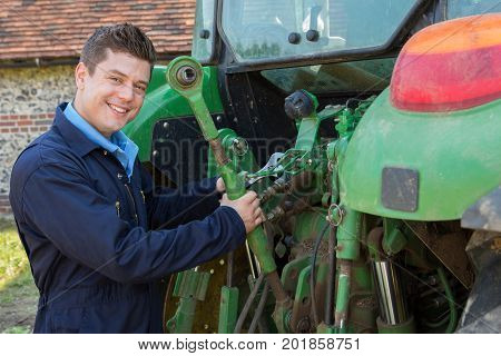 Portrait Of Mechanic Repairing Tractor On Farm