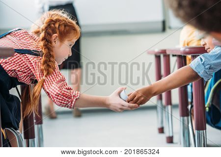 schoolgirls passing message in class on lesson