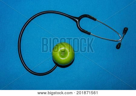 stethoscope and green apple on blue background