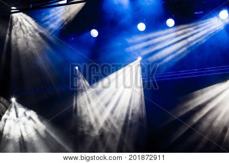 White and blue light rays from the spotlight through the smoke at the theater or concert hall. Lighting equipment for a performance or show.