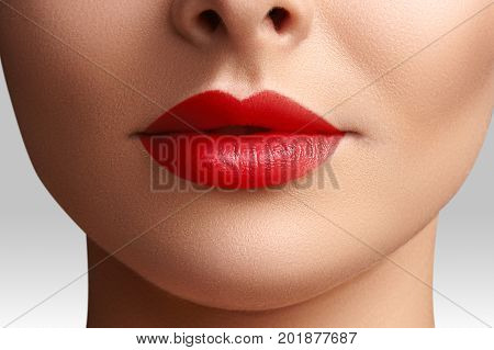 Cosmetics makeup and trends. Bright lip gloss and lipstick on lips. Closeup of beautiful female mouth with red lip makeup. Beautiful part of female face. Perfect clean skin in red light