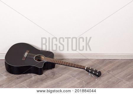 Black Classical Acoustic Guitar in an Empty Room lying on floor in front of the Wall with Copy Space extreme closeup