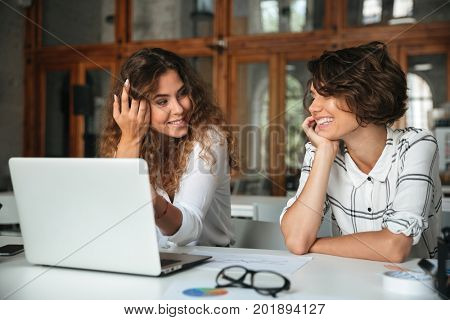 Two pretty happy women working by the laptop computer in co working office