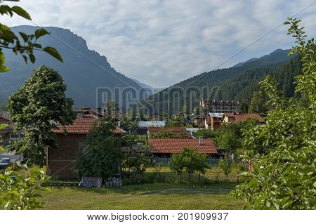 Scene with mountain top, forest, glade and residential district of bulgarian village Beli Iskar, Rila mountain, Bulgaria