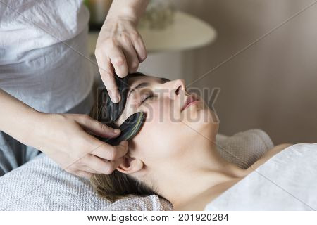 Young woman have face guasha treatment at asian beauty clinic