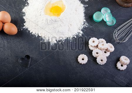 Flour eggs and canestrelli Italian shortbread cookies cooking utensils on black table