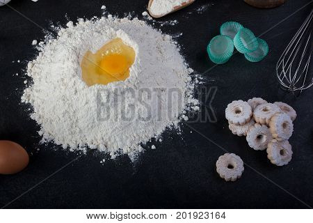 Flour eggs and canestrelli Italian shortbread cookies cooking utensils on black table