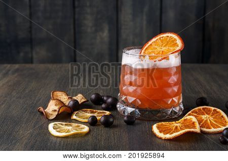 Cocktail on rustic wood background. Cold citrus alcohol beverage with tequila, blood orange juice and ginger beer, served with ice, citrons and chocolate snacks, copy space