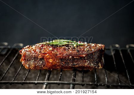 Hot spicy steak grilling on a summer barbecue over the hot coals garnished decorated with a branch of rosemary. Cooking food. close-up