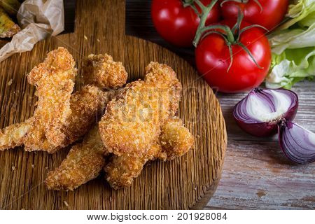 Chicken breast nuggets with vegetables on wooden background. Pile of crispy homemade baked chicken nuggets cooling. Top view. Close up.