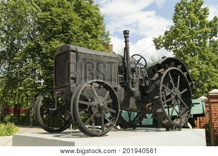 An old black wheeled tractor stands as a monument on a white pedestal closeup