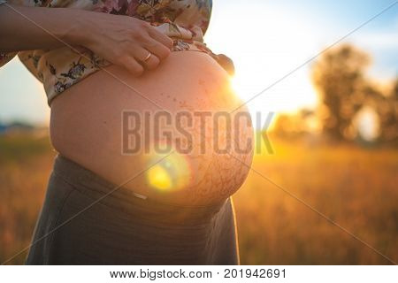 A beautiful pregnant woman on the beach touching her mehandi ornament belly with love and care at sunset lights summer evening