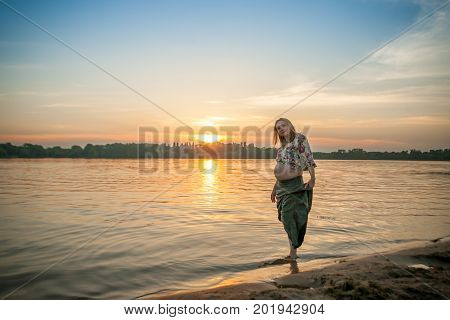 A pregnant beautiful woman on the river bank beach smiling with her mehandi ornament belly with love and care. Happy woman on sunset