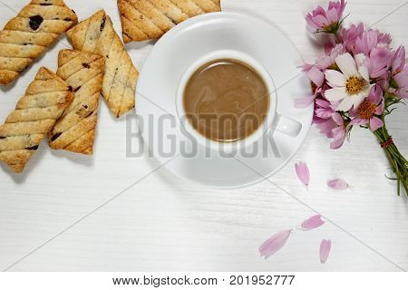 coffee with biscuits and flowers on a white table