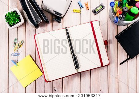 Top view workspace mockup on wooden background with blank notebook with copy space, pen, tacker, punch, clips and accessories. Overhead view. Flat lay, top view