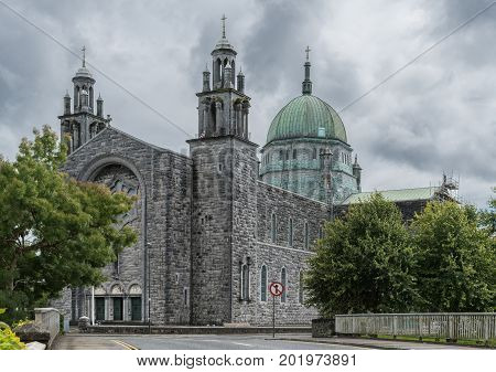 Galway Ireland - August 5 2017: Outside view of the Cathedral with green dome main entrance at nave flanked by two towers. Street scene with green trees on sides.