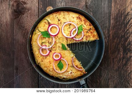 An overhead photo of a Spanish tortilla with potatoes and zucchinis in a tortillera, with a missing slice, and a place for text