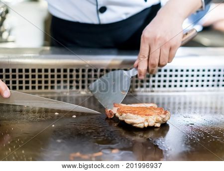 Hand Of Chef Cooking Chicken Steak On Hot Pan In Front Of Customers.