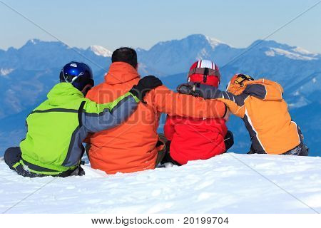 Padre e figli ammassati insieme nella neve sul versante di una montagna alta.