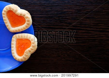 two heart shaped cookies in blue plate on wooden surface copyspace