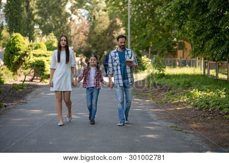 Happy Family Walking Down The Road Outside In The City Park. Family Is Holding Each Other Hands. The