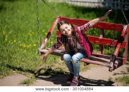 Smiling Little Girl With Long Pigtails Is On The Swing In The Park.she Is Smiling While Looking An T