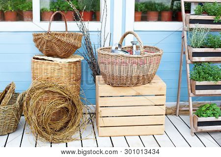 Wicker Baskets Next To The Garden Equipment Against The Wall Of A Blue Country House. Summer Seasona