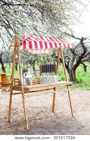 In The Park On The Green Lawn A Wooden Counter With A Lemonade. An Adorable Summer Lemonade Stand. C