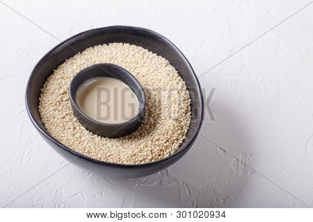 Tahini Sauce And Sesame Seeds In Black Bowls On White Background. Natural Paste Made From Sesame See