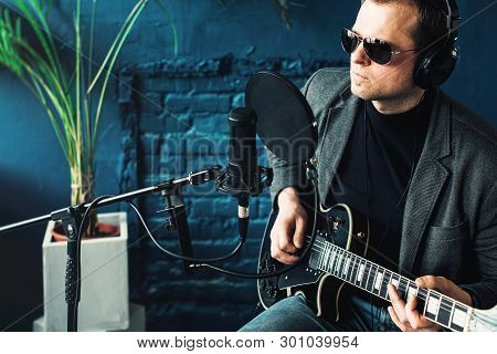 Close Up Of A Man Singer Sitting On A Stool In A Headphones With A Guitar Recording A Track In A Hom