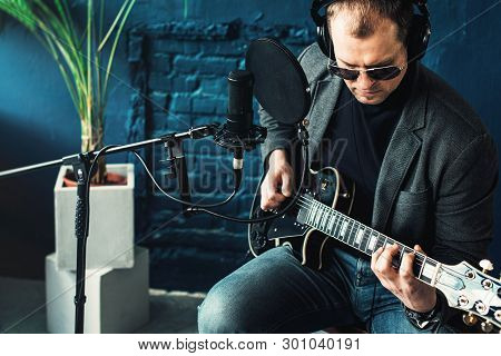 Close Up Of A Man Singer Sitting On A Stool In A Headphones With A Guitar Recording A Track In A Hom